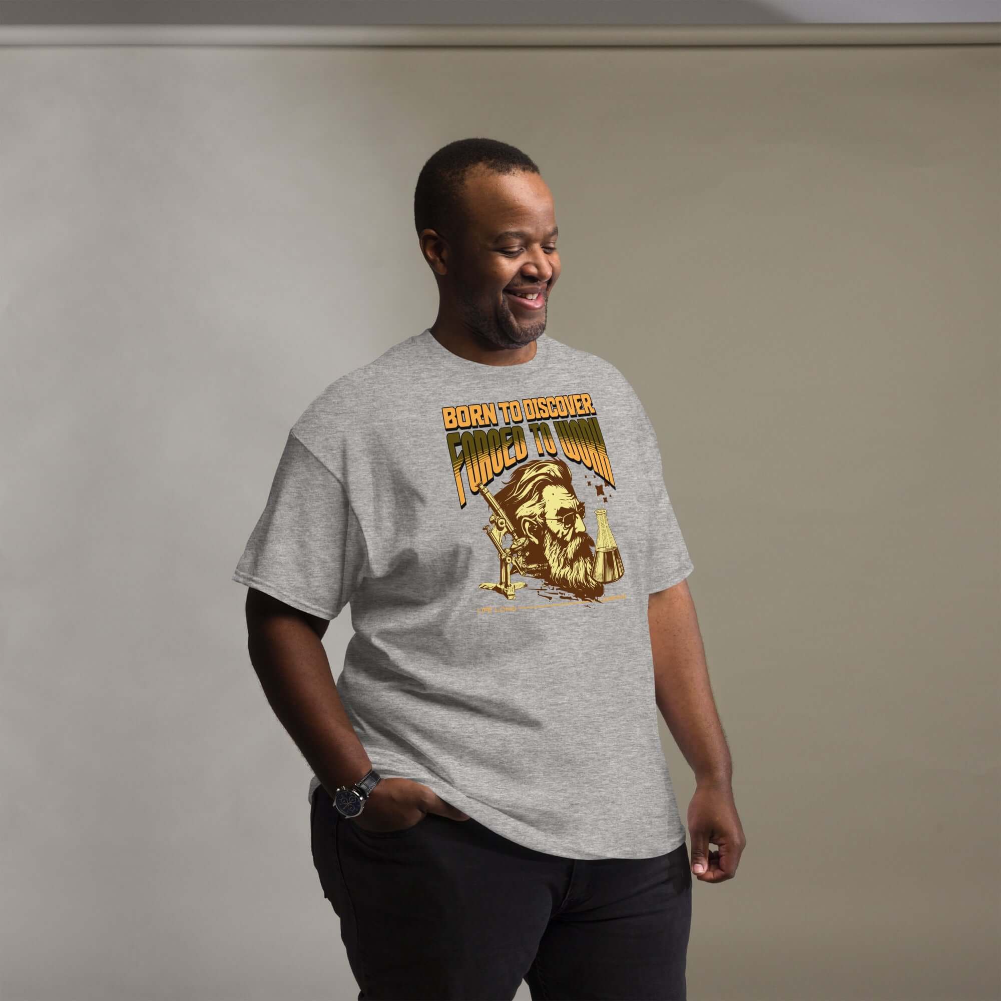 Man wearing gray 'Born to Discover, Forced to Work' t-shirt with vintage scientist illustration and humorous lament motif.
