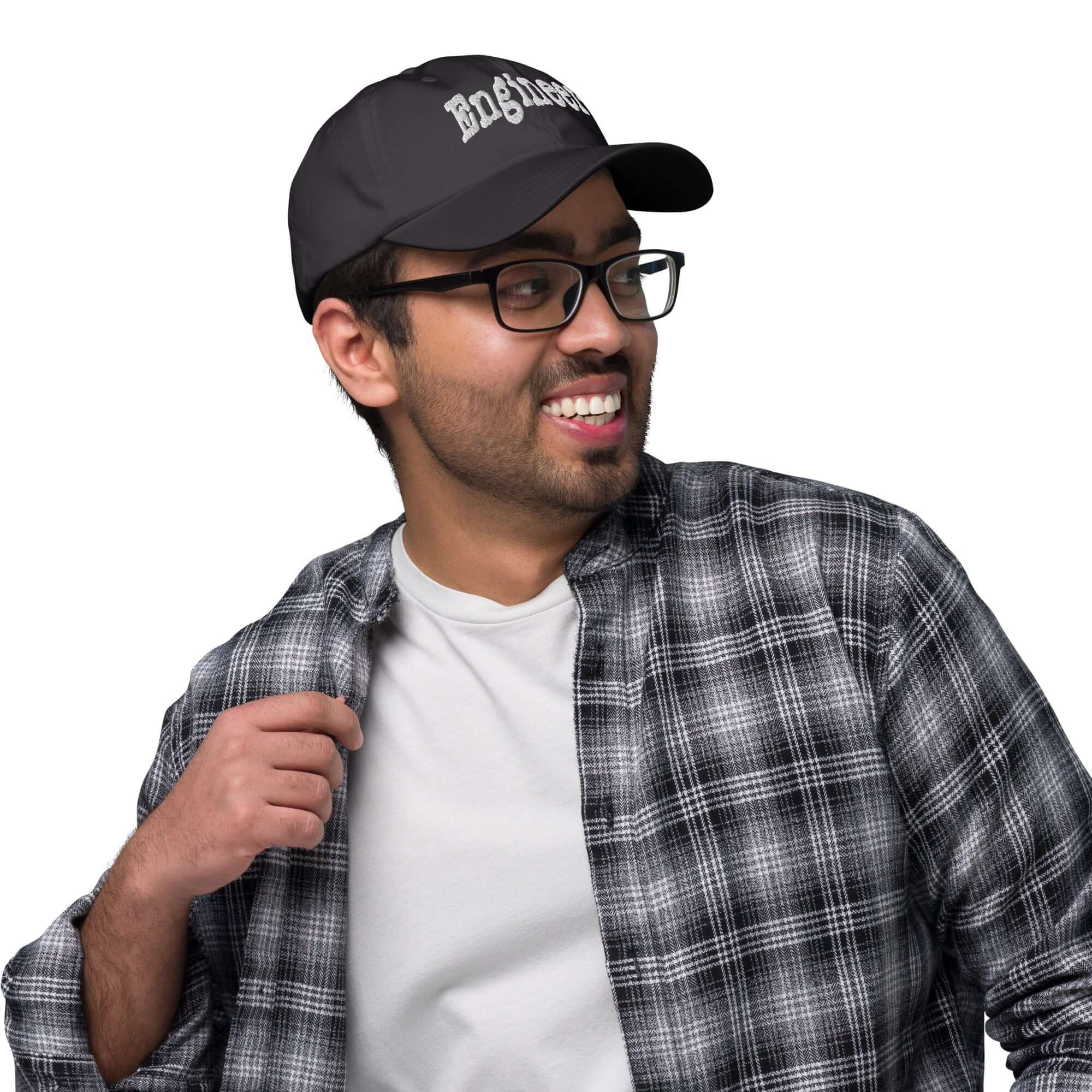 Man wearing "ENGINEER" baseball cap, epitome of problem-solving style, in casual plaid shirt and white tee, confidently smiling.
