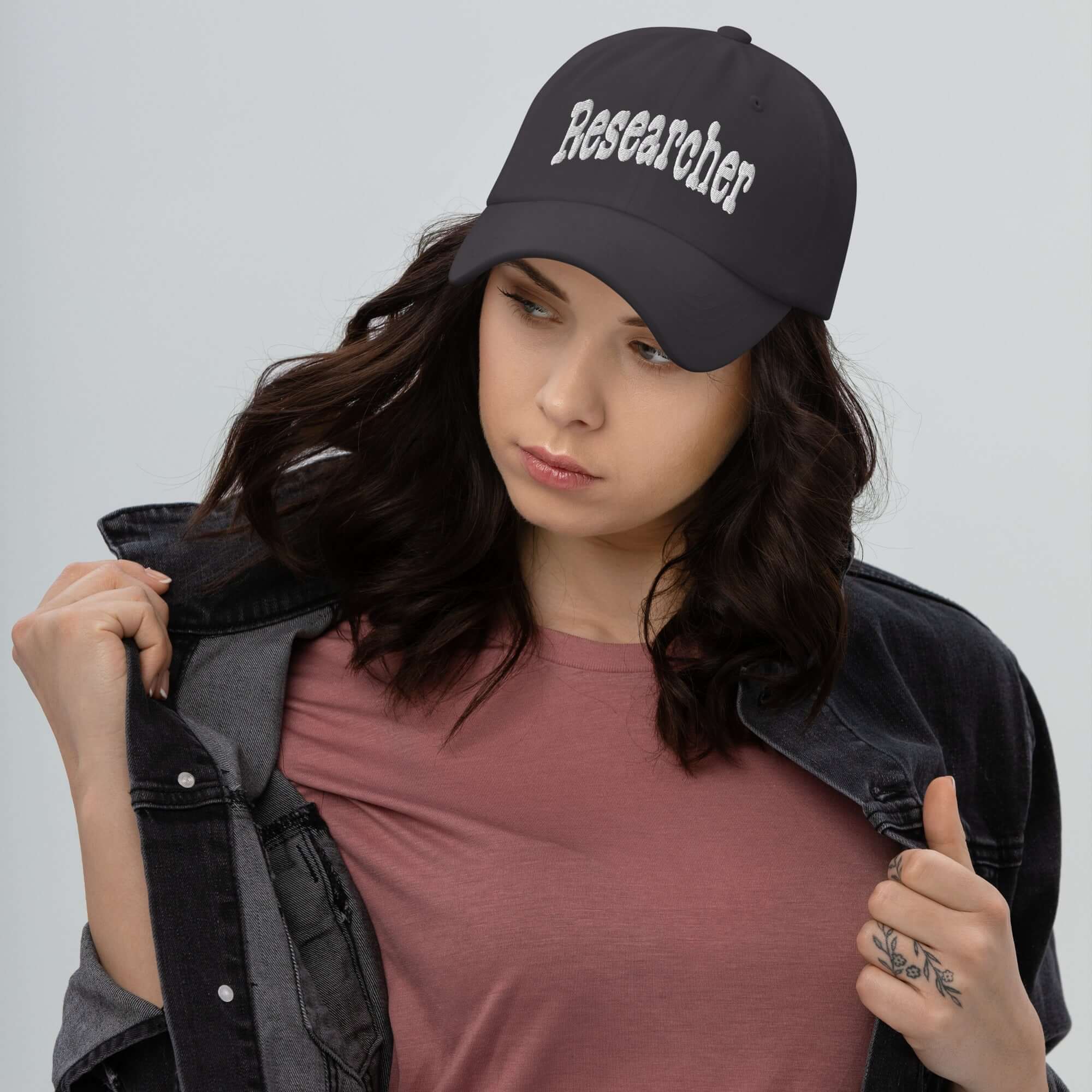 Woman wearing black 'Researcher' baseball cap, embodying professional curiosity and inquiry, against a neutral background.